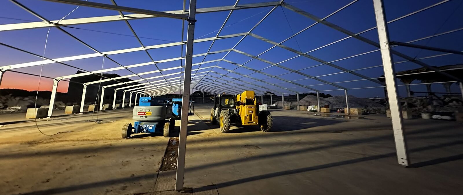 Large clear-span structure under construction at a mega-project jobsite at dusk.